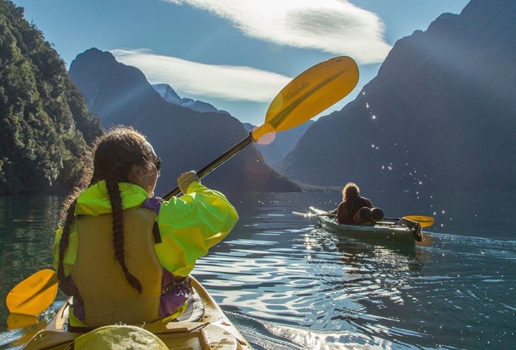 Three kayakers paddle through the Milford Sound on a sunny day from Milford Sound Lodge.