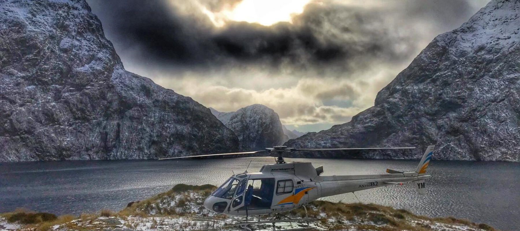 A helicopter sits on tussocks next Milford Sound from a scenic flight.