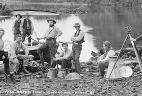A black and white photo of gold miners sit riverside in Milford Sound.