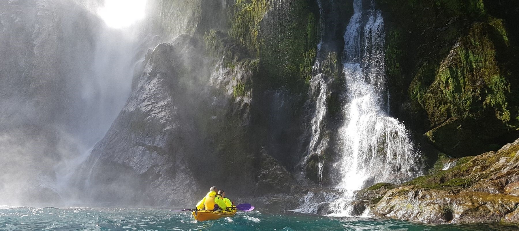 A double kayak heads towards a waterfall. One of the Milford Sound Lodge activities.