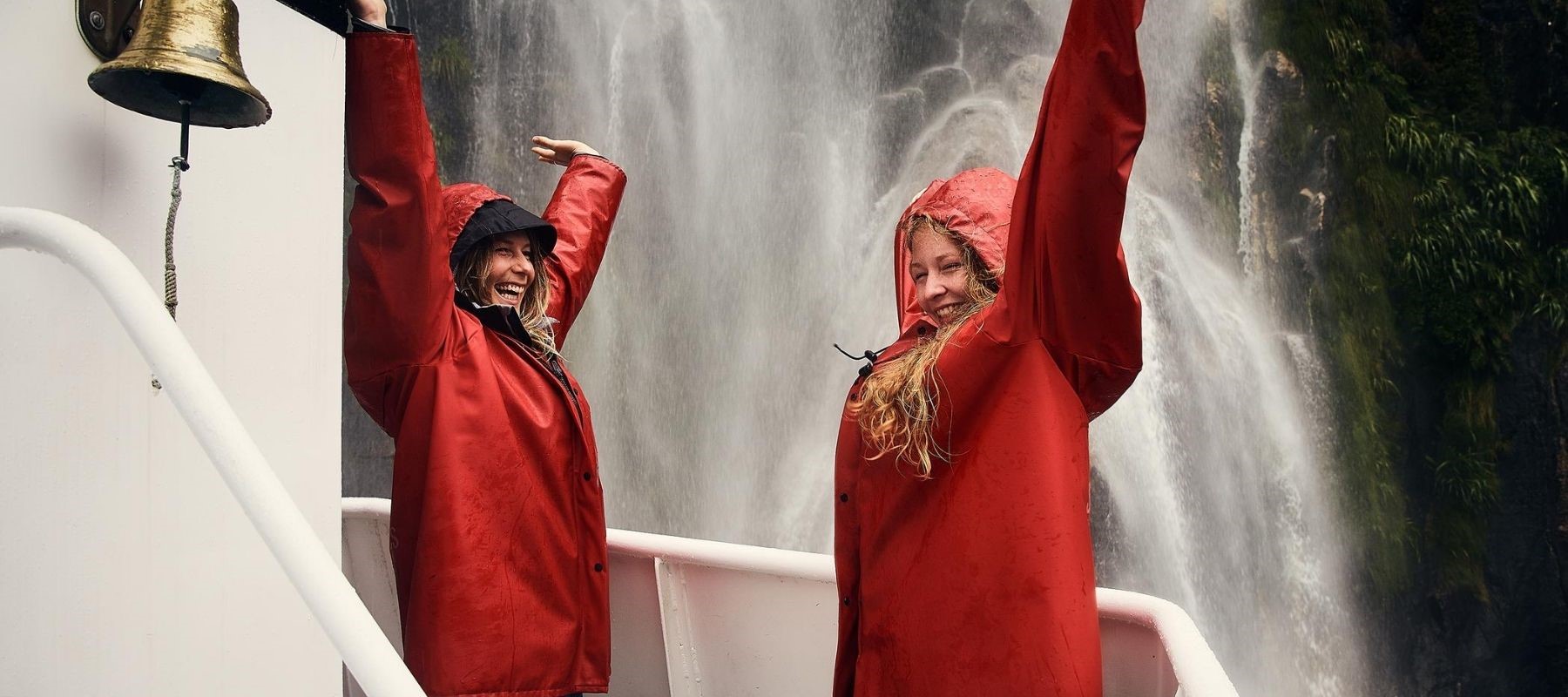 Two women enjoy waterfall spray from a Southern Discoveries boat tour from Milford Sound Lodge.