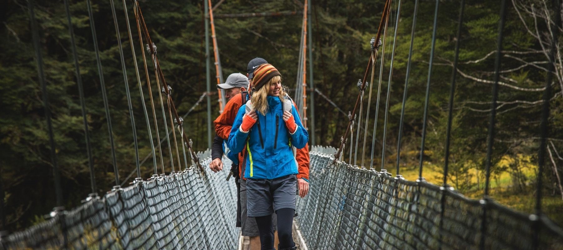 Three hikers stand on a bridge along the Milford Track. 