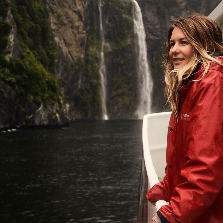 A young female enjoying a Milford Sound Cruise beside a waterfall.