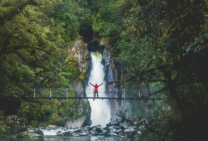 Hiker standing on a bridge overlooking a waterfall