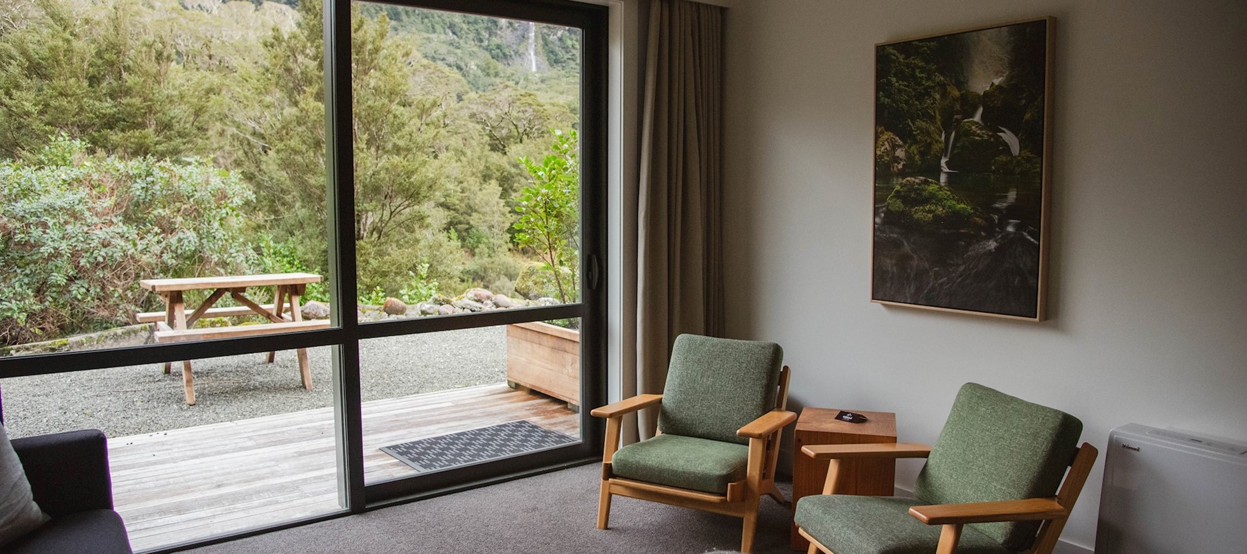 Two comfortable lounge chairs placed beside a large floor to ceiling window looking out at the native bush in Fiordland National Park 