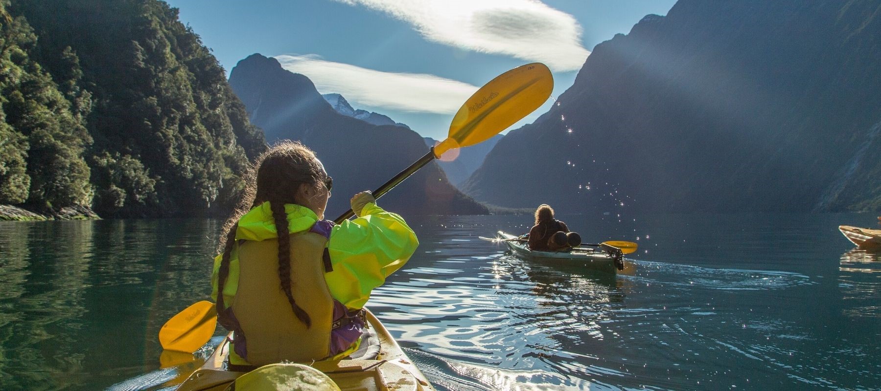 Three kayakers paddle through the Milford Sound on a sunny day from Milford Sound Lodge.