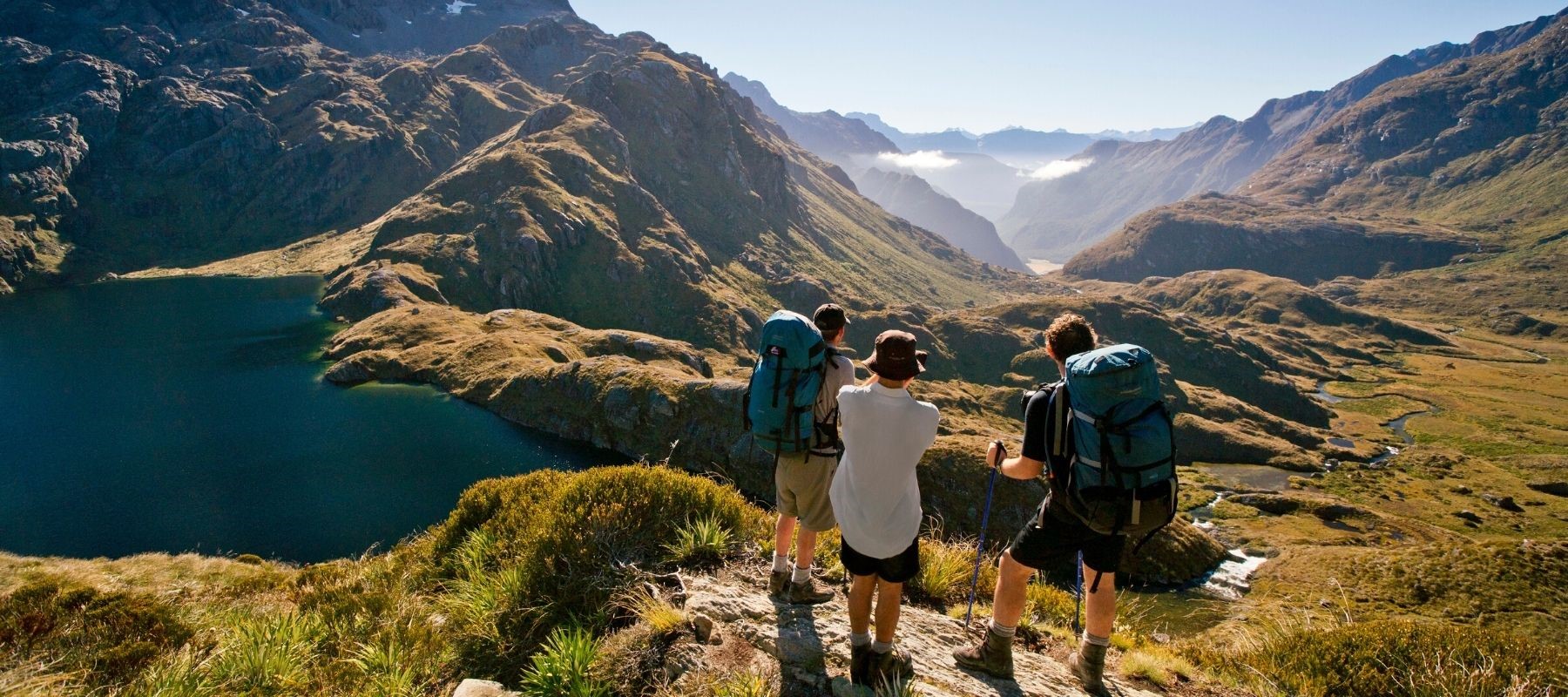 Three hikers look over the valley atop on the Routeburn Track, Milford Sound.