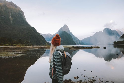 Girl standing with Red winter hat and backpack on looking over Milford Sound out at Mitre Peak