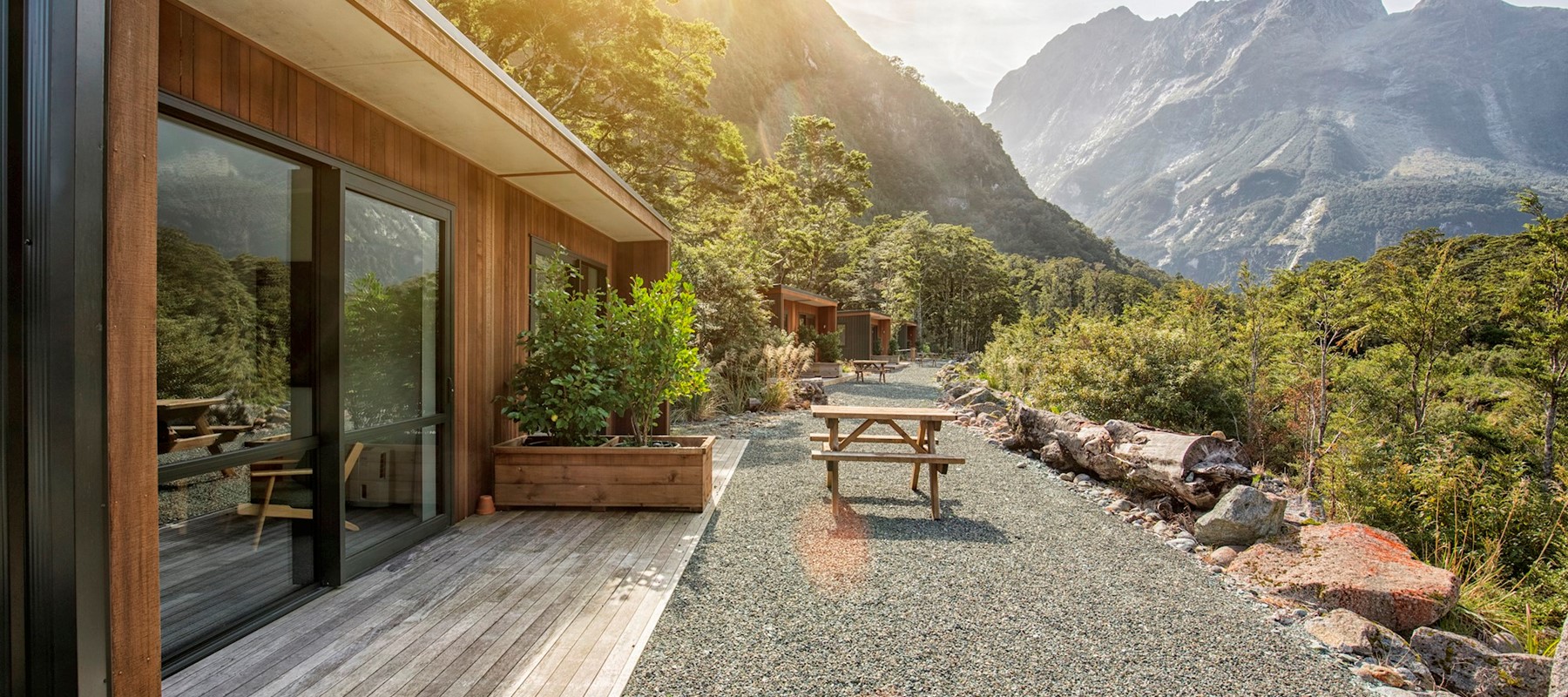 Sunrise streaming over the mountains onto the Milford Sound Lodge Chalets, lighting up the native green bush and the natural wooden chalets 