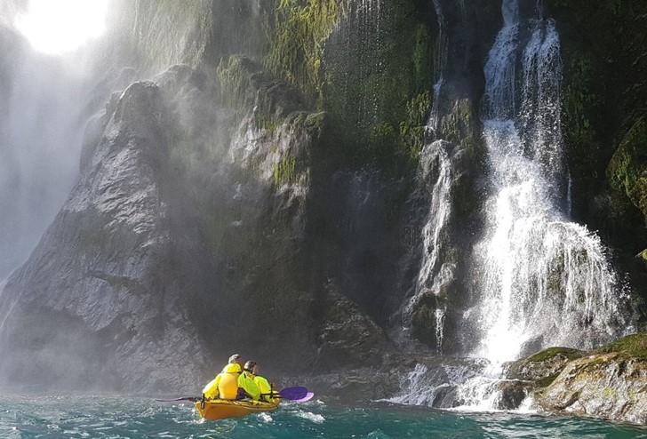 A double kayak heads towards a waterfall. One of the Milford Sound Lodge activities.