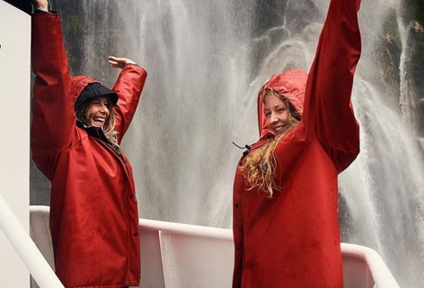 Two women enjoy waterfall spray from a Southern Discoveries boat tour from Milford Sound Lodge.