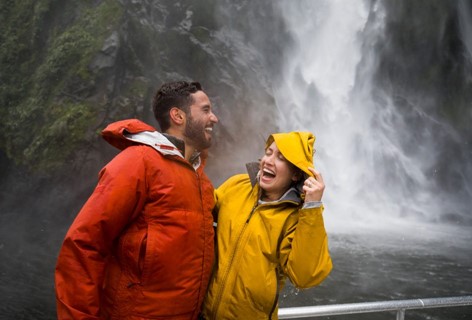 A couple laugh as they're splashed by a cascading waterfall on a Milford Sound Cruise.