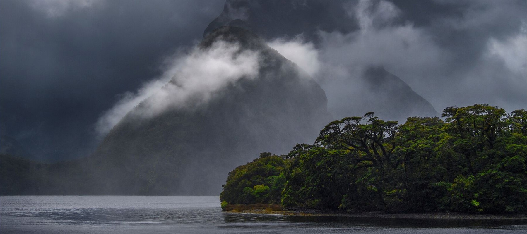 Clouds hang in front of mountain peaks in Milford Sound near Milford Sound Lodge.