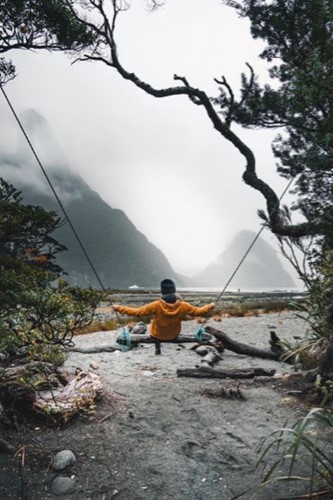 A child enjoys a swing on the banks for Milford Sound with mountain peaks in the background.